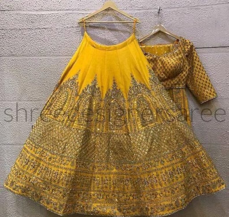 May include: A yellow lehenga with gold embroidery and sequins. The skirt is full and flowing, and the top is a fitted choli with short sleeves.
