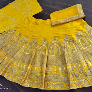 May include: A yellow skirt with intricate gold embroidery and embellishments. The skirt is made of a soft, flowing fabric and has a flared silhouette. The skirt is paired with a matching yellow dupatta, which is a long scarf that is often worn with Indian clothing.