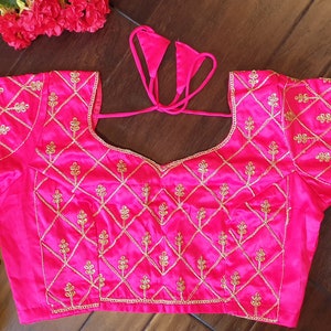 May include: A pink satin blouse with gold embroidery featuring a diamond pattern and floral motifs. The blouse has a tie-up back.