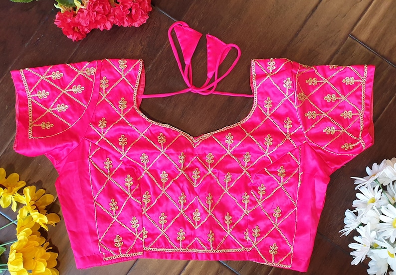 May include: A pink satin blouse with gold embroidery featuring a diamond pattern and floral motifs. The blouse has a tie-up back.