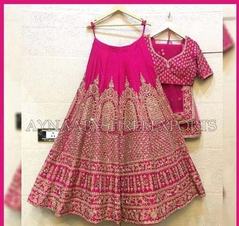 May include: A pink and gold embroidered lehenga with a matching choli. The lehenga is a traditional Indian garment worn by women for special occasions.