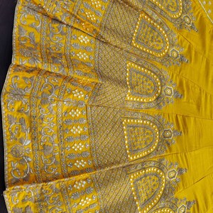 May include: A yellow skirt with intricate gold and white embroidery. The skirt has a circular shape and is decorated with a floral pattern.