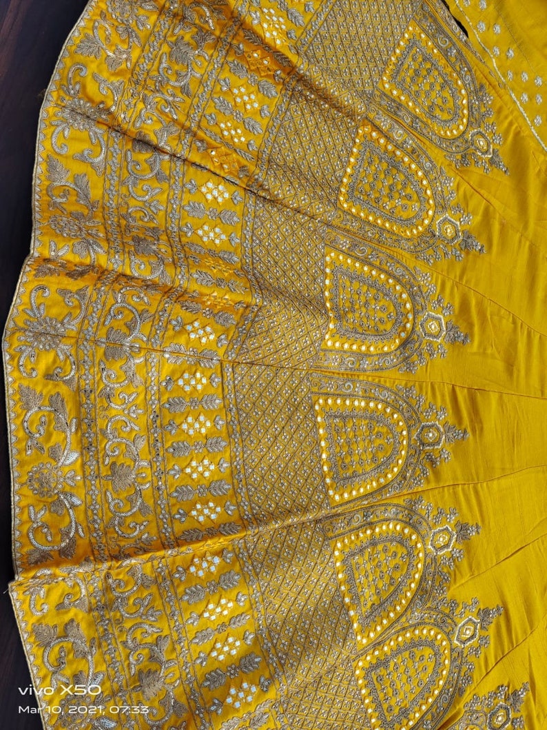 May include: A yellow skirt with intricate gold and white embroidery. The skirt has a circular shape and is decorated with a floral pattern.
