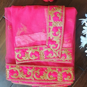 May include: A pink sheer fabric with gold embroidered trim. The trim features a floral design.