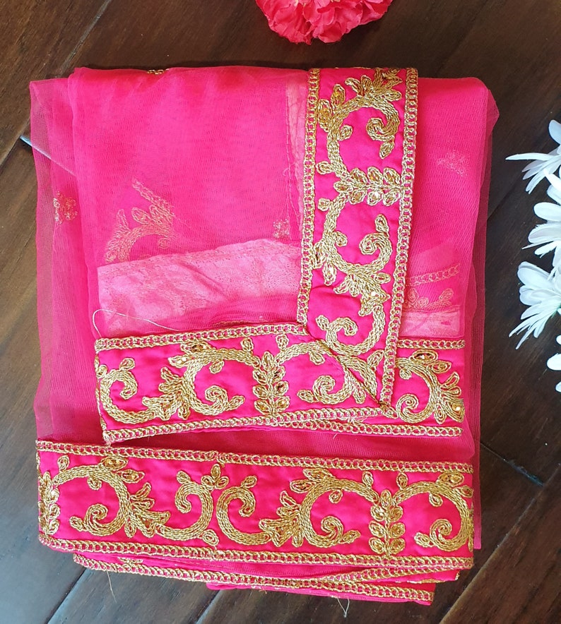 May include: A pink sheer fabric with gold embroidered trim. The trim features a floral design.