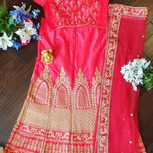 May include: A pink and gold embroidered lehenga with a matching dupatta. The lehenga has a fitted bodice with short sleeves and a flowing skirt. The dupatta is a sheer fabric with a gold embroidered border.
