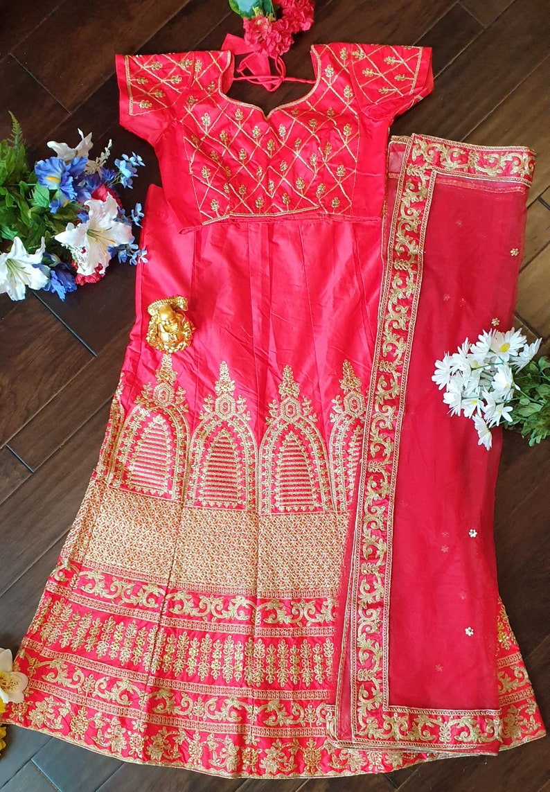 May include: A pink and gold embroidered lehenga with a matching dupatta. The lehenga has a fitted bodice with short sleeves and a flowing skirt. The dupatta is a sheer fabric with a gold embroidered border.