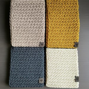 Könnte beinhalten: Vier gehäkelte Quadrate in verschiedenen Farben: Beige, Senfgelb, Dunkelgrau und Weiß. Die Quadrate sind mit einem einfachen Stichmuster gearbeitet und haben eine strukturierte Optik.