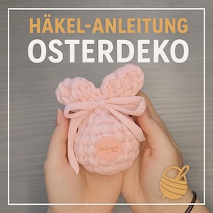 Puede incluir: Una decoración de conejito de Pascua de crochet rosa con un lazo. El conejito está siendo sostenido en las manos de una persona. El texto "Handmade" es visible en el conejito.