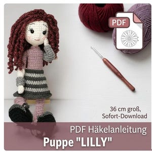 May include: A crochet doll named Lilly with curly dark red hair, wearing a mauve long-sleeved top and a gray and white striped skirt. The set includes a brown crochet hook, two balls of yarn, and a PDF pattern icon with the text 36 cm groß, Sofort-Download, PDF Häkelanleitung, Puppe LILLY.