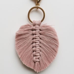 May include: A pink macrame feather keychain with a gold metal key ring and clasp.