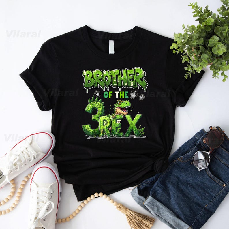 May include: Black t-shirt with a green graphic that reads "BROTHER OF THE 3 REX." The design features a cartoon dinosaur and the number 3. The shirt is displayed with white sneakers, denim shorts, and sunglasses.