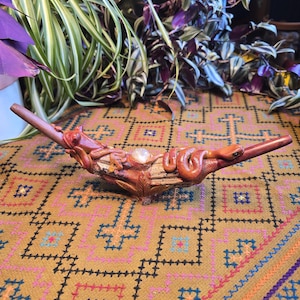 May include: A handcrafted wooden sculpture featuring a coiled orange snake and a small lizard. The sculpture is adorned with a clear crystal and rests on a patterned fabric. The piece is approximately 12 inches long.