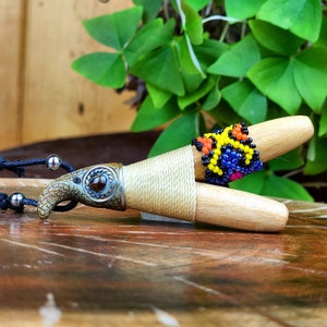 May include: A wooden pendant with a beaded design in yellow, orange, blue, and black. The pendant is attached to a brown cord and has a ceramic bird head with a brown eye.