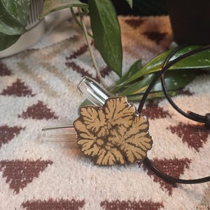 May include: A brown ceramic pendant with a floral design hangs from a black cord. The pendant is on a brown and white patterned surface.