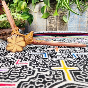 May include: A wooden smoking pipe with a carved bird head and a four-leaf clover design. The pipe is resting on a colorful patterned fabric.