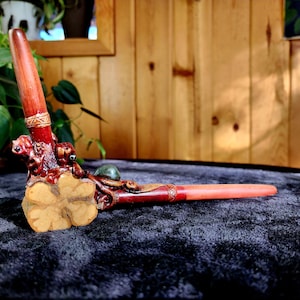 May include: A wooden pipe with intricate carvings and a green stone accent. The pipe is resting on a dark gray surface.