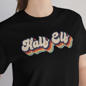 May include: A black t-shirt with a retro-style graphic that says "Half Elf" in rainbow colors.