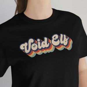 May include: A black t-shirt with a retro-style graphic that says "Void Elf" in rainbow colors.