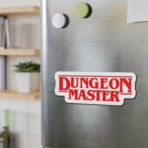 May include: White refrigerator magnet with red text that reads "DUNGEON MASTER" in a stylized font.