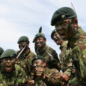 May include: A group of soldiers in camouflage uniforms and green berets are shouting and holding knives. They are wearing face paint and have a serious expression on their faces.