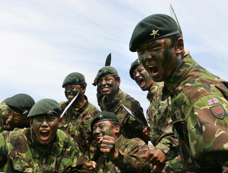 May include: A group of soldiers in camouflage uniforms and green berets are shouting and holding knives. They are wearing face paint and have a serious expression on their faces.