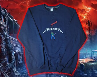 May include: Navy blue sweatshirt featuring the word "MUNSON" in a stylized font with a lightning bolt design. A cartoon figure playing a guitar is below the text. The sweatshirt has a crew neck and long sleeves.