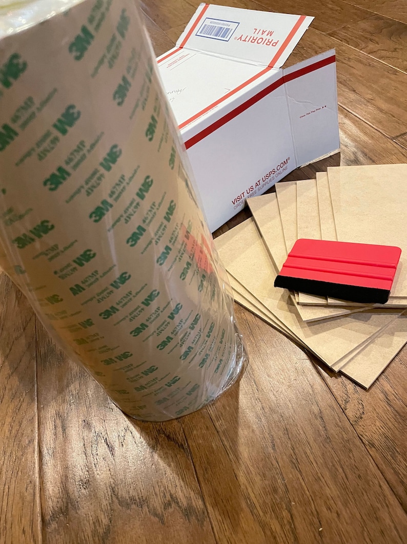 K&ouml;nnte beinhalten: Eine Rolle braunes 3M Klebeband mit gr&uuml;ner Beschriftung, ein roter Rakel und mehrere Bl&auml;tter braunes Papier.