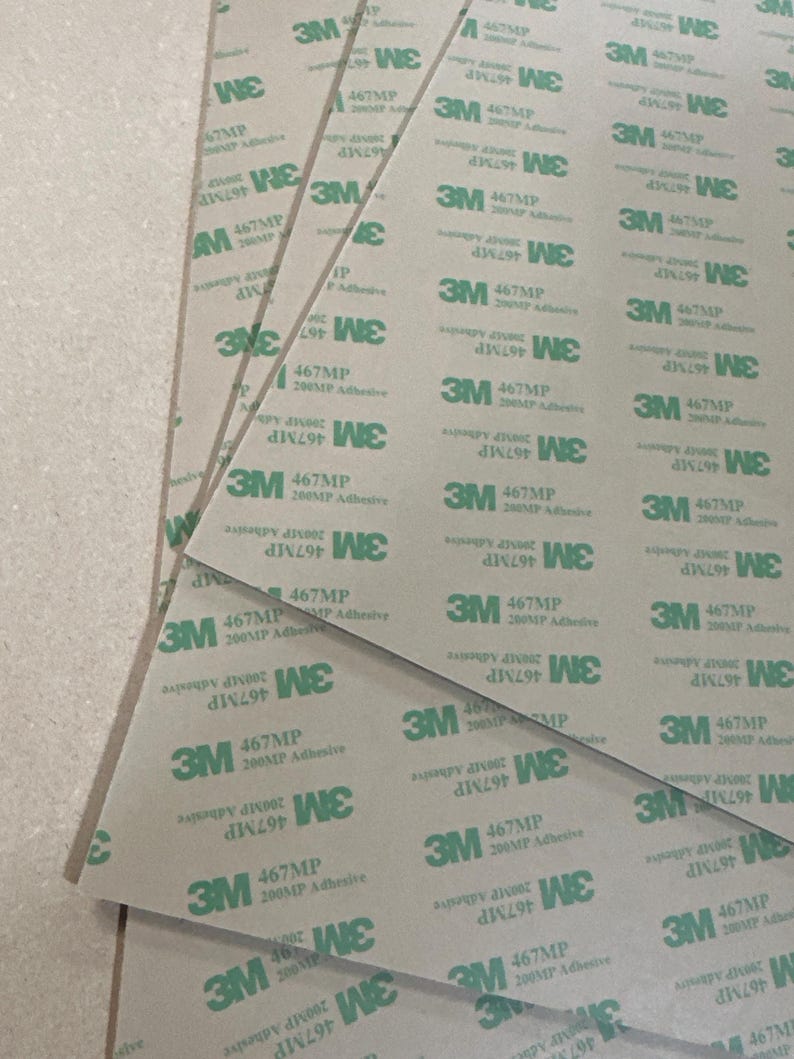 May include: Close-up of several sheets of brown paper with green 3M 467MP 200MP Adhesive labels. The labels are printed with the text "3M 467MP 200MP Adhesive" and "DIN 1297 WE".