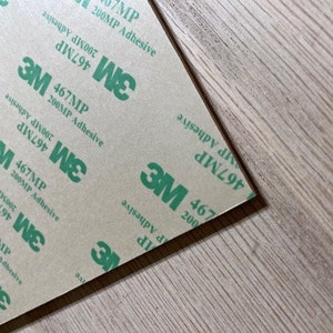 May include: Close-up of a sheet of brown paper with repeating green text that reads "3M 467MP 200MP Adhesive".