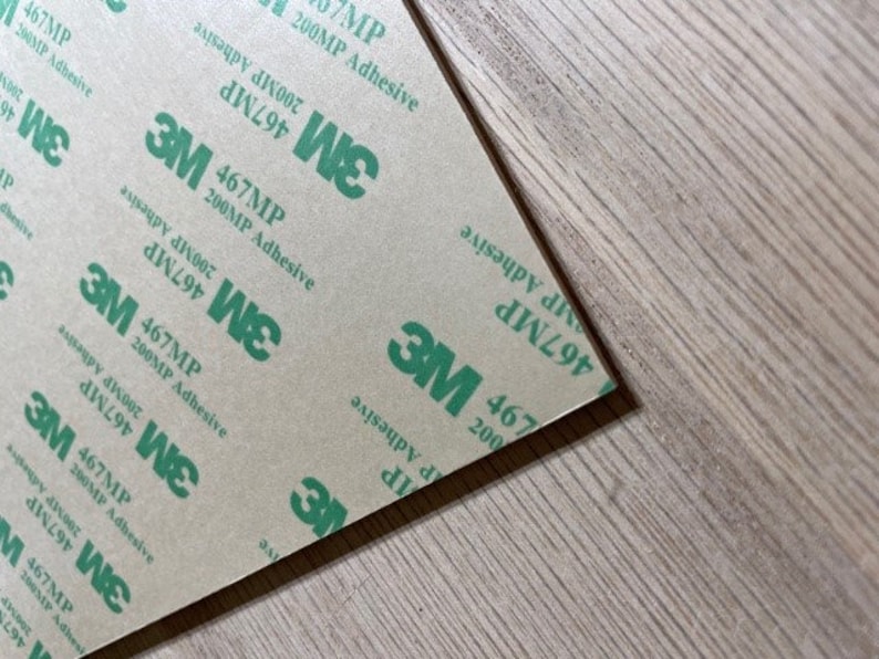 May include: Close-up of a sheet of brown paper with repeating green text that reads "3M 467MP 200MP Adhesive".