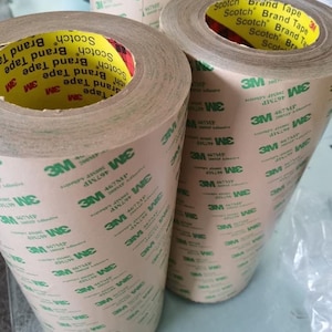 K&ouml;nnte beinhalten: Drei Rollen braunes Klebeband mit gr&uuml;nem Text, der "Scotch Brand Tape" und "3M 467MP 200MP Adhesive" lautet.