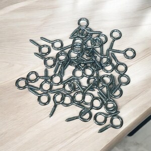 May include: A pile of silver eyelet screws with a screw thread and a small loop at the top.