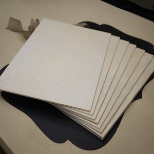 May include: A stack of eight unfinished wood squares, each measuring approximately 12 inches by 12 inches. The wood is a light beige color with a natural wood grain pattern.