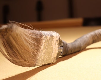 May include: A close-up of a paintbrush with a worn wooden handle and a frayed bristle head. The brush is covered in dried paint.