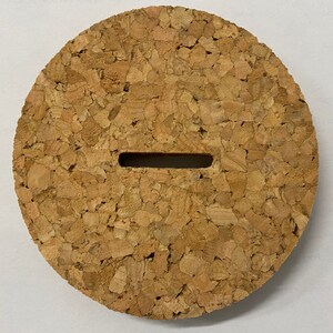 Puede incluir: Un tap&oacute;n redondo de corcho con una ranura rectangular cortada en el centro. El corcho es de color marr&oacute;n claro y tiene una textura rugosa.