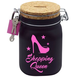 Puede incluir: Huchas de cer&aacute;mica negra con tapa de corcho y cerradura con llave. La hucha tiene un zapato de tac&oacute;n alto rosa y estrellas con el texto "Shopping Queen" en la parte delantera.