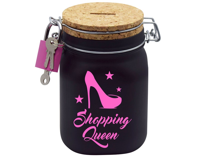 Puede incluir: Huchas de cer&aacute;mica negra con tapa de corcho y cerradura con llave. La hucha tiene un zapato de tac&oacute;n alto rosa y estrellas con el texto "Shopping Queen" en la parte delantera.