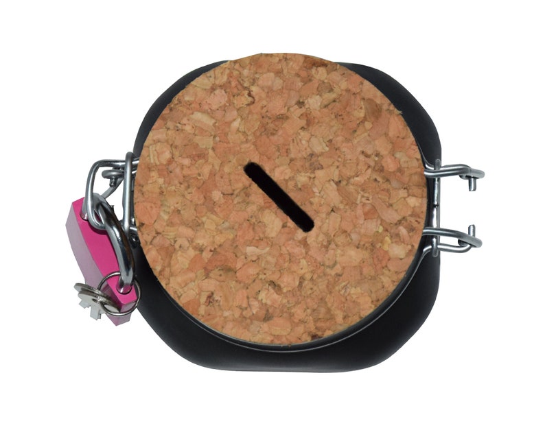Puede incluir: Un tarro negro con tapa de corcho y un candado rosa. La tapa tiene una ranura para insertar dinero.