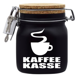 Op de afbeelding: Zwarte keramische pot met een kurken deksel en een metalen sluiting. De pot heeft een wit koffiekopje met stoom en de tekst "Kaffee Kasse" erop gedrukt.