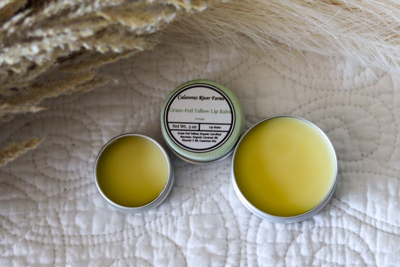 May include: Three small silver tins of lip balm. The center tin has a green label that reads "Calaveras River Farms Grass-Fed Tallow Lip Balm Orange Net Wt. .5 oz. Lip Balm Grass-Fed Tallow, Organic Certified Beeswax, Organic Coconut Oil, Vitamin E, Oil of Essential Oil."