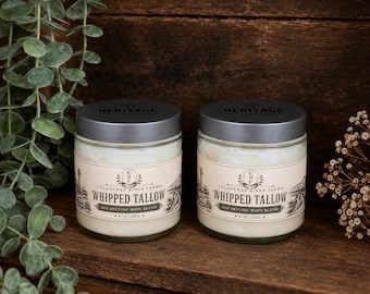 May include: Two clear glass jars filled with white whipped tallow body cream, each topped with a dark gray lid. The labels read Calaveras River Farms, Whipped Tallow, Age Defying Body Blend, and 4 oz | 113 g, featuring a vintage-style illustration.
