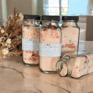 May include: Three glass jars filled with pink Himalayan salt bath soaks. Each jar has a label with the text "Bath Salts Lavender Magnesium Sulfate Citric Acid Himalayan Salt Essential Oil Rosehip Oil".