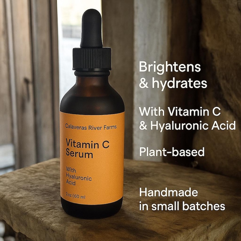 May include: A brown glass bottle of Vitamin C Serum with a black dropper. The label is orange with white text that reads "Vitamin C Serum" and "With Hyaluronic Acid". The bottle is 2 fl oz (60 ml). The text on the right says "Brightens & hydrates" and "Plant-based".