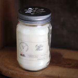May include: A clear glass jar candle with a silver lid and a label that reads "Coffee House." The candle is filled with a creamy white wax. The label also includes the text "CALAVERAS RIVER FARMS" and other details.