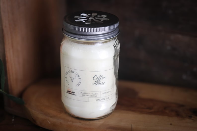 May include: A clear glass jar candle with a silver lid and a label that reads "Coffee House." The candle is filled with a creamy white wax. The label also includes the text "CALAVERAS RIVER FARMS" and other details.