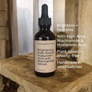 May include: A dark brown glass bottle with a black dropper, labeled "Brightening Kojic Acid & Hyaluronic Acid with Niacinamide Serum." The label also states the product is plant-based, cruelty-free, and handmade in small batches. The bottle contains 2 fl oz / 60 mL.
