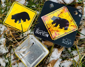 May include: Yellow and black metal pin-back buttons featuring a bear silhouette, similar to a road sign. One button is loose, revealing the pin back. Another is on a black card with the text "Metal Pin-Back Button" and "Made by Firefly's Dream".