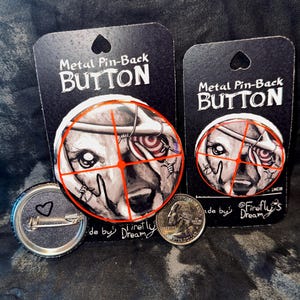 Op de afbeelding: Twee metalen pin-back knopen met een honden gezicht ontwerp, een met een hartvormige pin. De knopen staan op zwarte kaarten met de tekst "Metal Pin-Back BUTTON". Een munt ligt naast de knopen ter referentie van de grootte.
