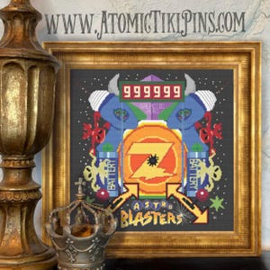 Puede incluir: Un bordado de punto de cruz enmarcado con un diseño de videojuego retro que muestra el texto "ASTRO BLASTERS". La obra de arte incluye una pantalla de puntuación, un emblema central naranja y amarillo, y elementos gráficos azules y rojos. Se ve la web "WWW.ATOMICTIKIPINS.COM".